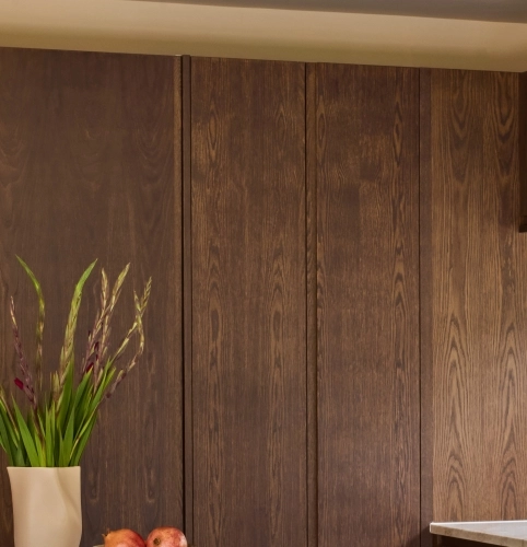 Wooden kitchen cabinet with vertical grooves and two metal handles, set against a wall. The bottom of the image shows part of a white and brown marble countertop.