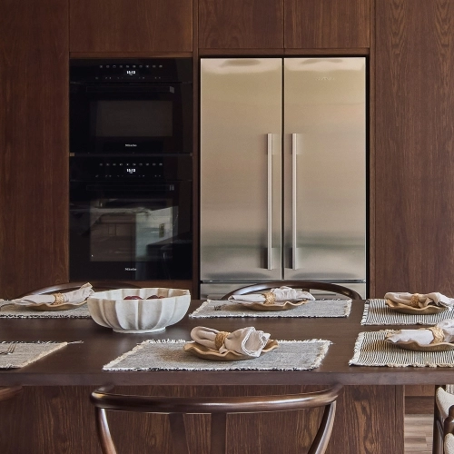 A kitchen counter area with a white marble backsplash featuring black veining, a farmhouse sink with a brass faucet, a blue cabinet, and a wooden countertop in the foreground. A decorative jar is near the sink