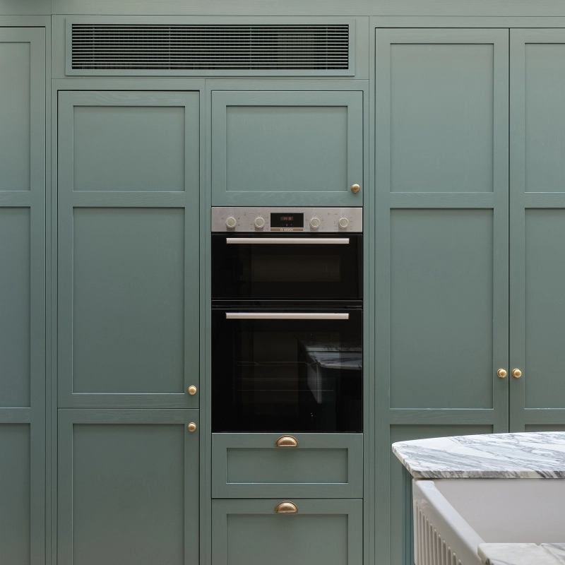 Light wood kitchen cabinets with gold hardware, a white marble countertop, and a brass faucet. Bottles, a brush, and a small radio sit on the counter. The backsplash is white subway tile.