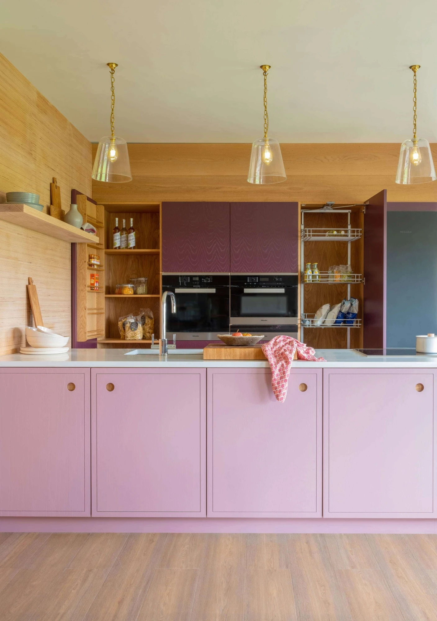 Oak ply wall paneling echoes the symmetry of the Ladbroke handle detailing, adding warmth & natural texture to the vibrant pink & purple kitchen.