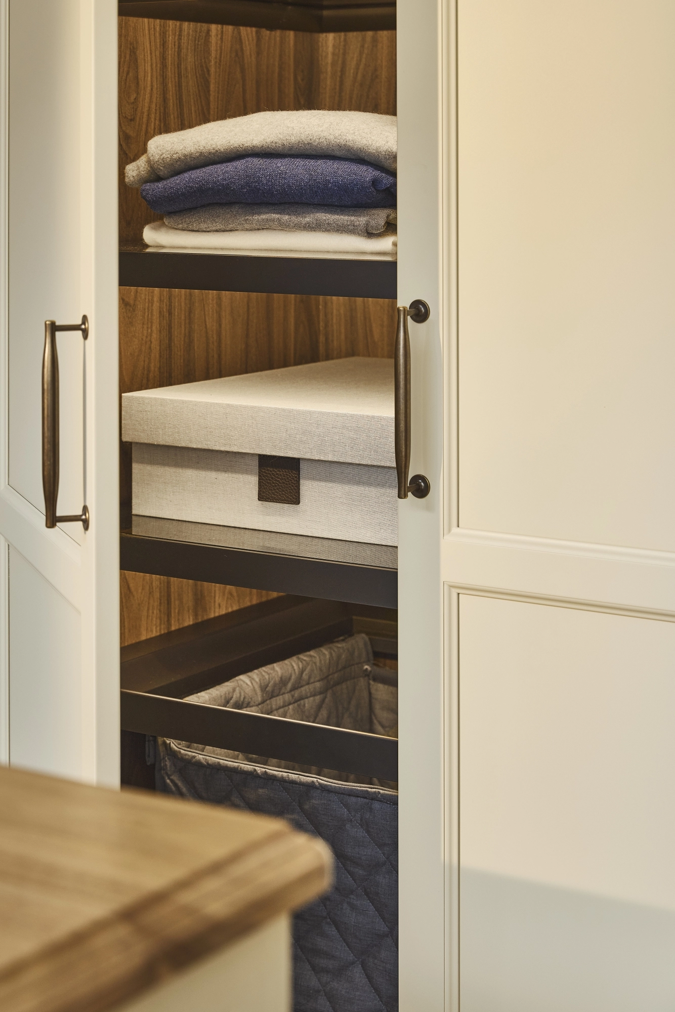 Cream-colored cabinet doors with dark metal handles, featuring a simple panel design. The edge of a wooden countertop is visible in the lower left corner of the image