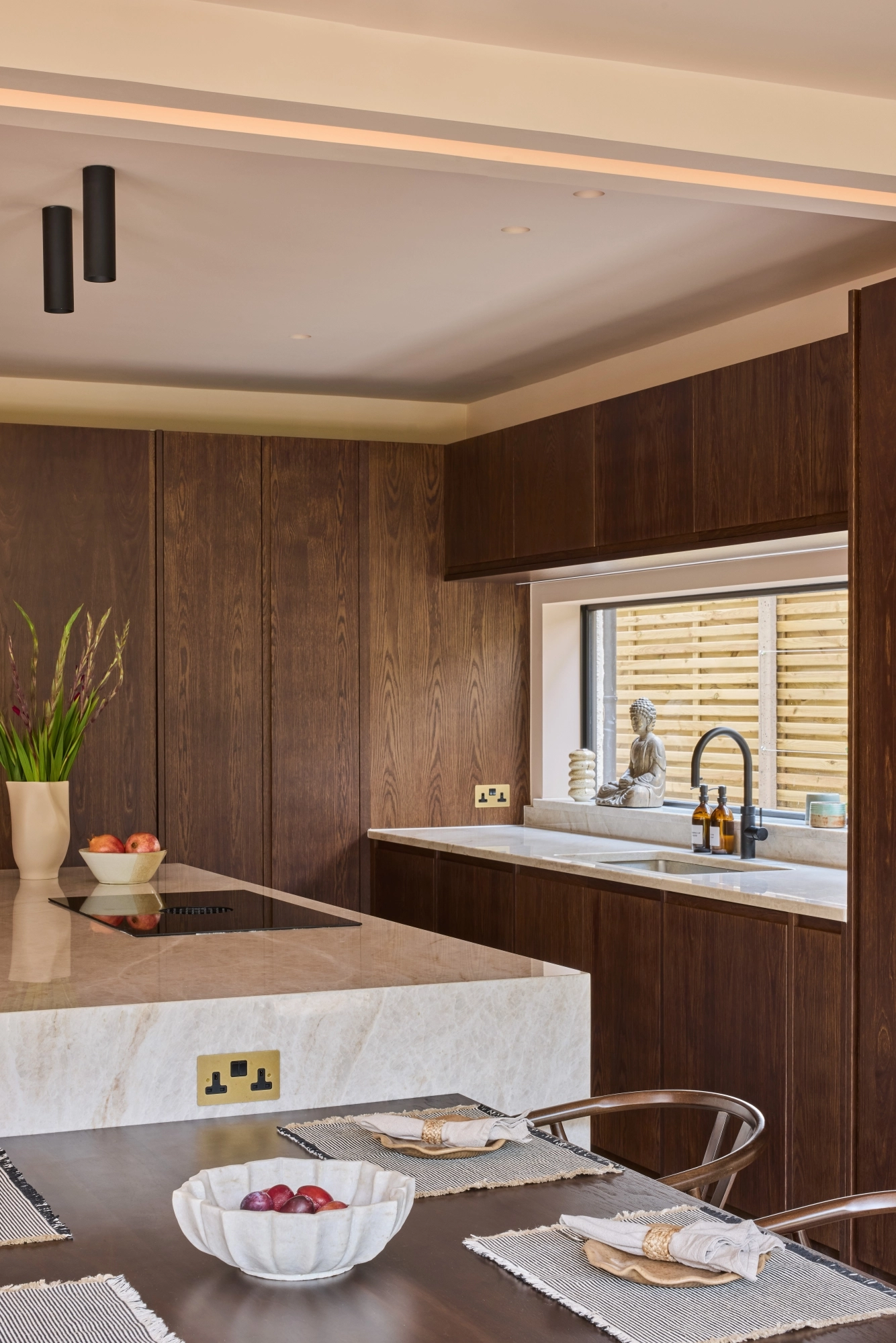 A wooden cabinet with glass doors displaying ceramic dishes, bowls, and a jug. Below is a light blue drawer set with a marbled countertop. Warm lighting highlights the textures and tones of the ceramics and wood