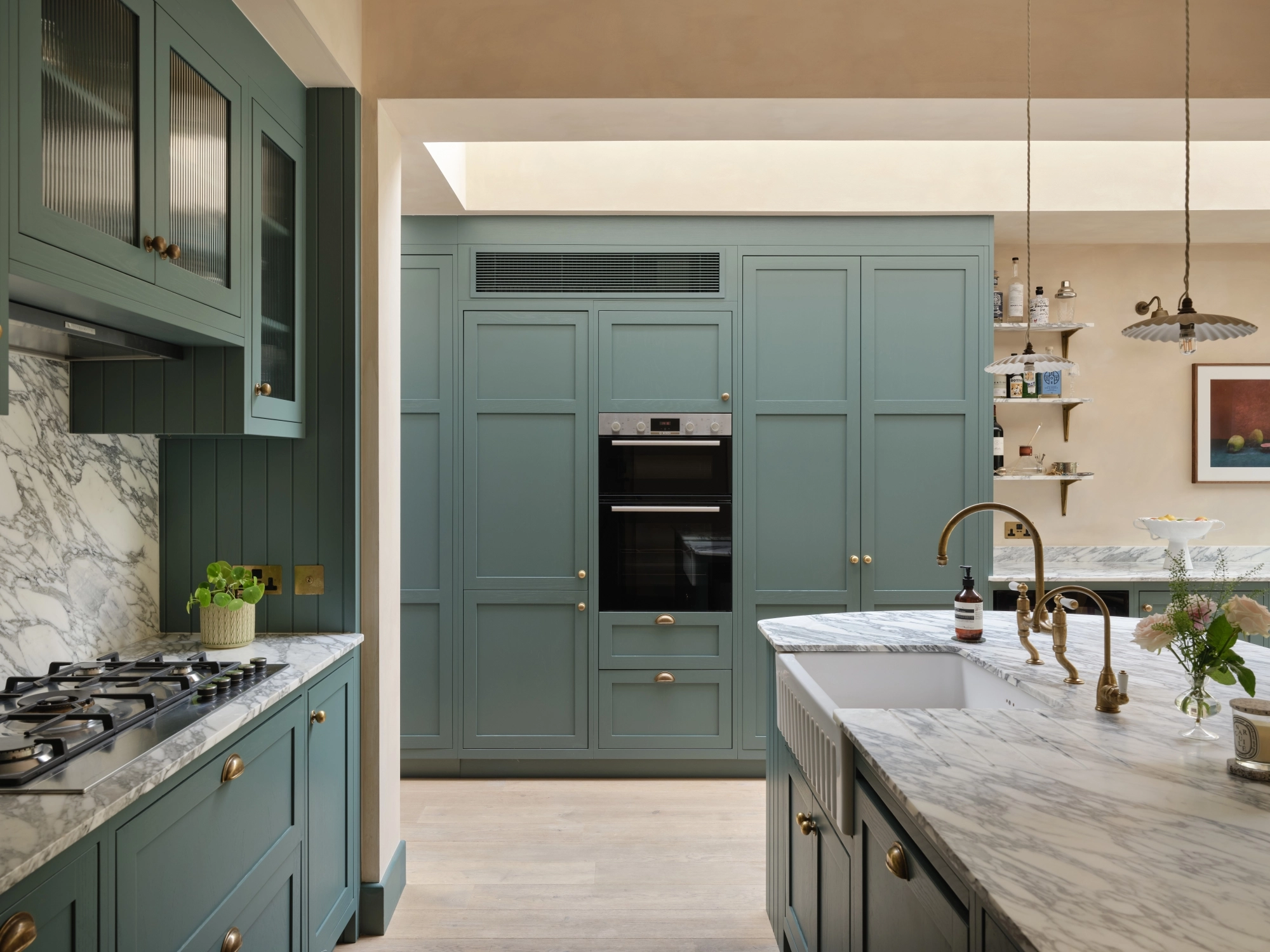 Close-up of a wooden cabinet with two open doors featuring round, textured metal knobs. Inside, there are neatly stacked plates with gold rims. The cabinet is set on a marbled surface